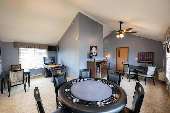 A poker table is surrounded by chairs in a room with a television and a clock on the wall.