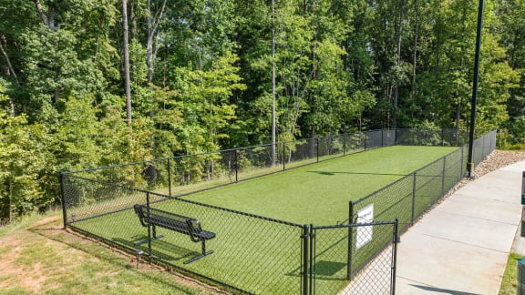 a tennis court with a bench and trees in the background