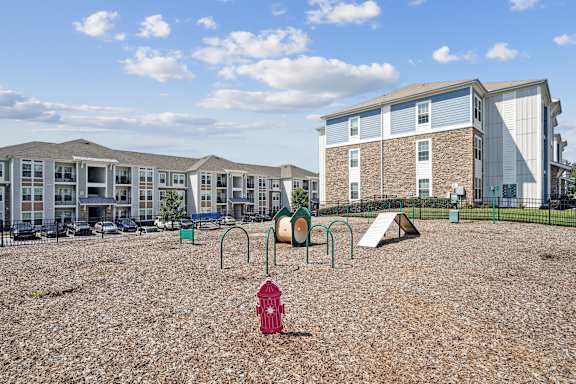 A playground with a red fire hydrant in the foreground and apartment buildings in the background.