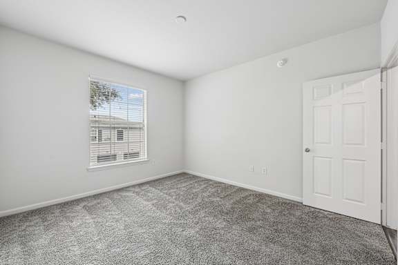 A room with a carpeted floor and a window with blinds.