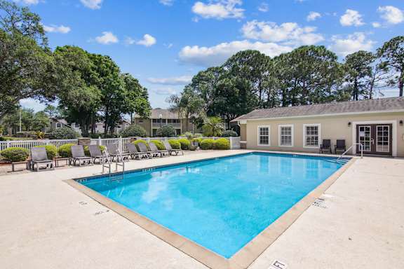 A large swimming pool surrounded by trees and chairs.