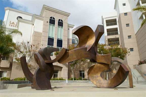 A large, abstract, metallic sculpture sits in front of a building with the sign "La Crosse.".