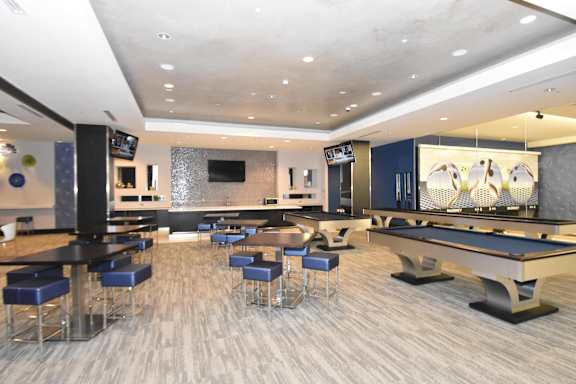 A pool table is in the middle of a room with bar stools.