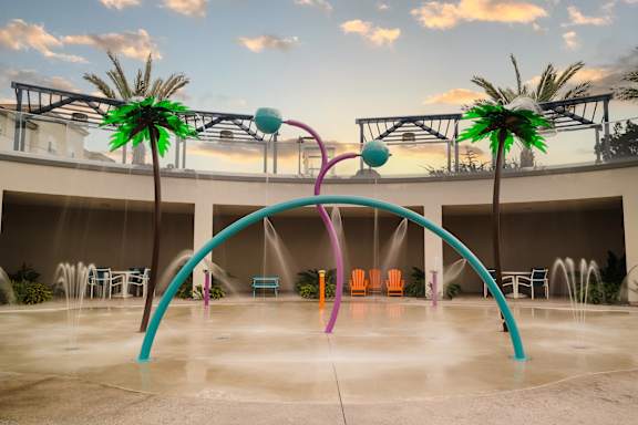 A water fountain with a purple arch and a green palm tree.