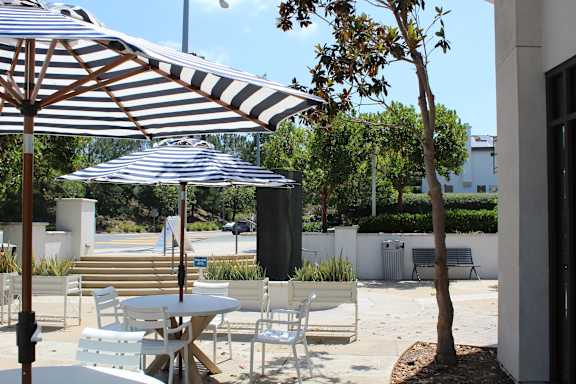Outdoor patio dining with striped umbrellas and seating at Torrey Gardens Apartments, California