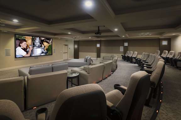 A row of seats are arranged in a room with a large screen on the wall.