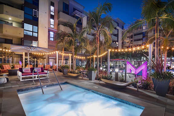 Twilight pool deck with palm trees and string lights at Metropolis Apartments, California