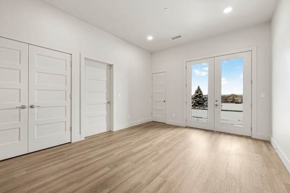 A room with white walls and wooden flooring, with a view of a tree through a window.