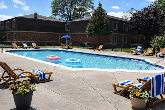 A pool surrounded by chairs and umbrellas with a building in the background.