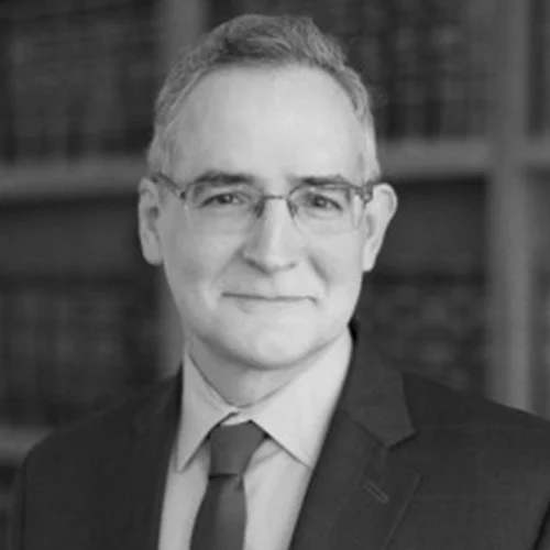 a man in a suit and tie standing in front of a bookshelf