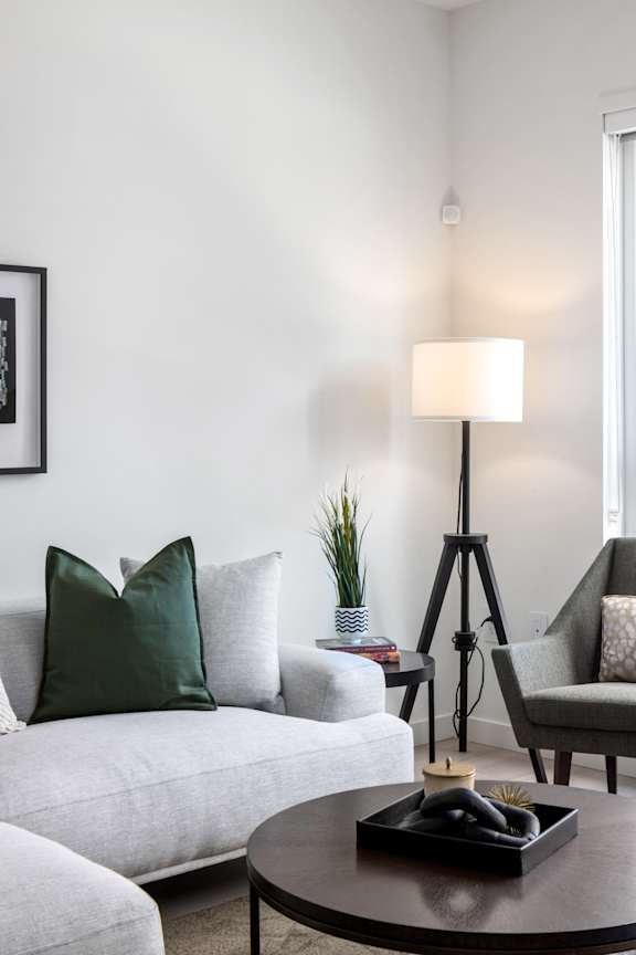 A living room with a grey couch, a small table with a black tray and candle, and a floor lamp.