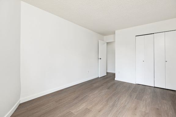 A room with white walls and wooden flooring with two white cupboards.