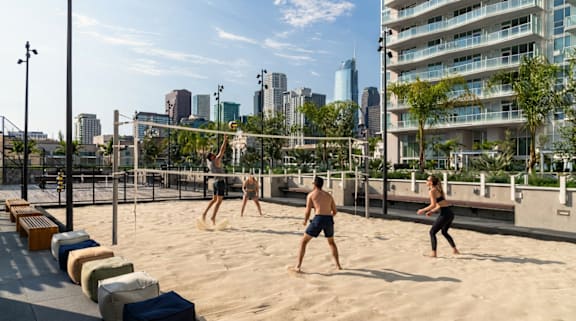 A group of people playing volleyball on a sandy court with a city skyline in the background. at Olympic + Hill Apartments, Apartments, Los Angeles, CA