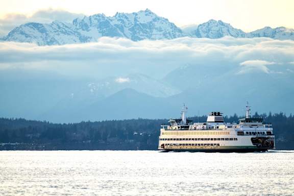 A large white boat is sailing on the water in front of a snowy mountain range.