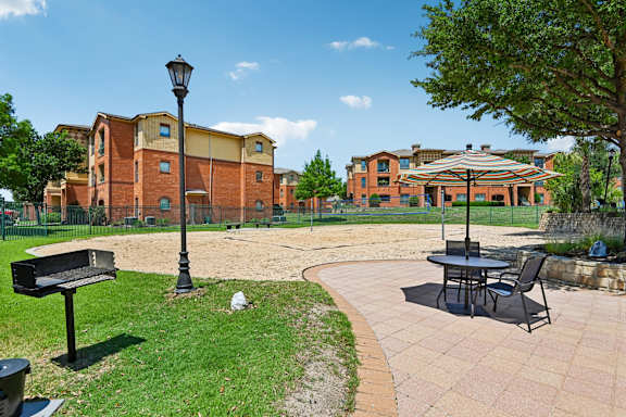A sunny day at a park with a bench, lamp post and a table with chairs.
