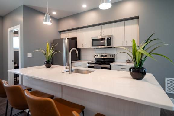 A modern kitchen with a white countertop and orange chairs.