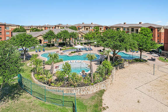 A large swimming pool surrounded by a fence and trees in a residential area.