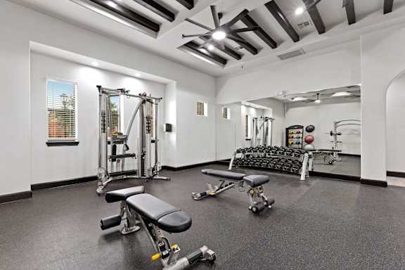 A spacious gym with a variety of equipment including a squat rack, bench, and dumbbells.