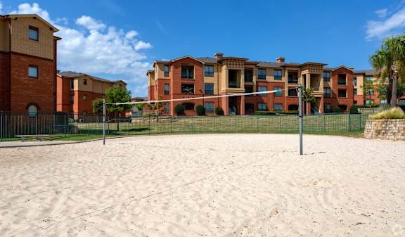 A sandy area in front of a building with a fence.