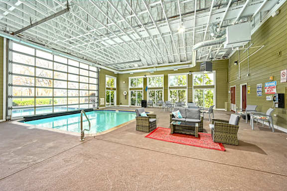 A large indoor swimming pool with a glass ceiling and a patio area with chairs and tables.