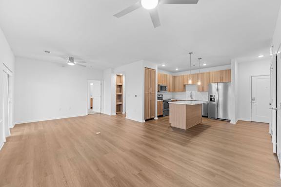 A spacious room with wooden flooring and a kitchen area in the background.