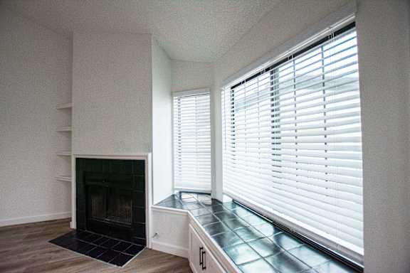 A fireplace with a black grate is in a room with a window covered in white blinds.