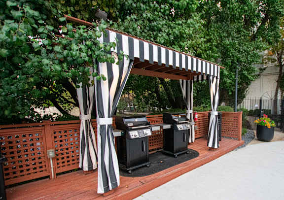 A striped canopy is over a grill and trash cans.