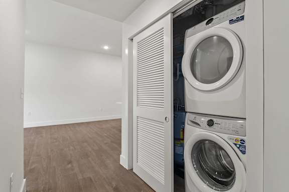 A white washing machine is in a white laundry room.