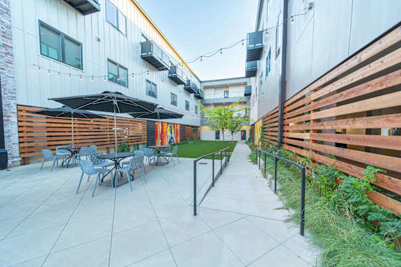 A patio with chairs and umbrellas is surrounded by buildings.