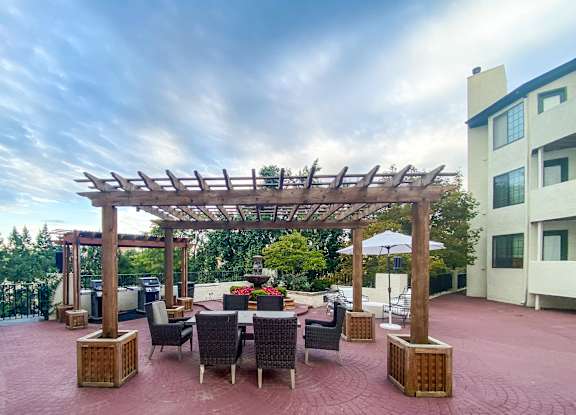 A patio with a table and chairs under a wooden pergola.