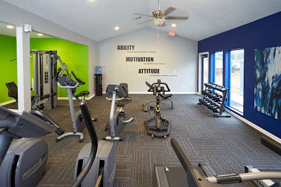 A gym with a green wall and a sign that says "Ability Motivation Attitude".