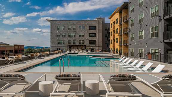 A pool surrounded by lounge chairs and buildings in the background.