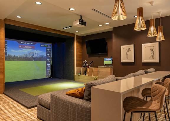 A room with a couch, chairs, and a large screen displaying a golf game.