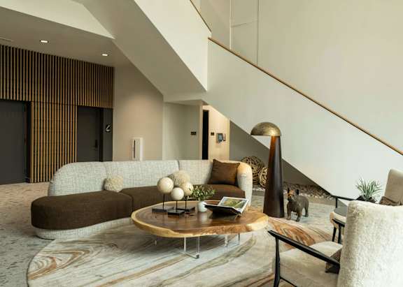 A living room with a brown sofa, a round wooden table, and a white chair.