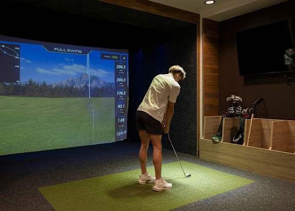 A woman is playing golf in a room with a screen showing a golf course.