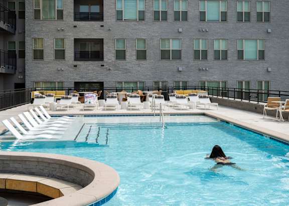 A person swims in a pool with a building in the background.