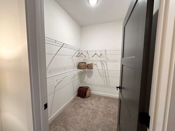 A small, empty room with a carpeted floor and a closet with clothes hanging on a rod.