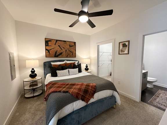 A bedroom with a bed, a ceiling fan, and a painting on the wall.