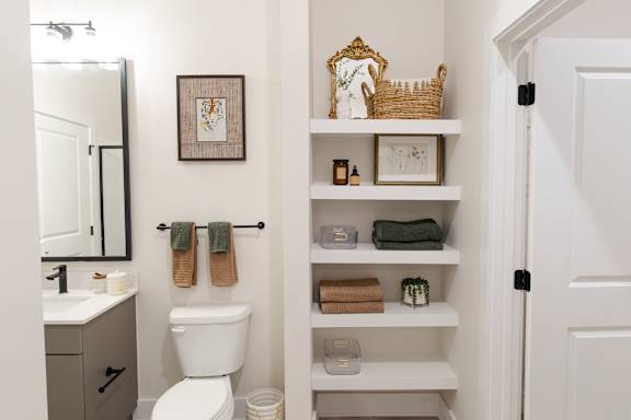 A bathroom with a toilet, sink, and shelves with towels and other items.