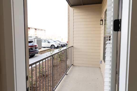 A balcony with a metal railing and a view of a parking lot.