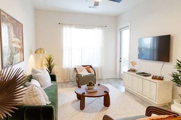 A living room with a green couch, a wooden coffee table, and a flat-screen TV mounted on the wall.