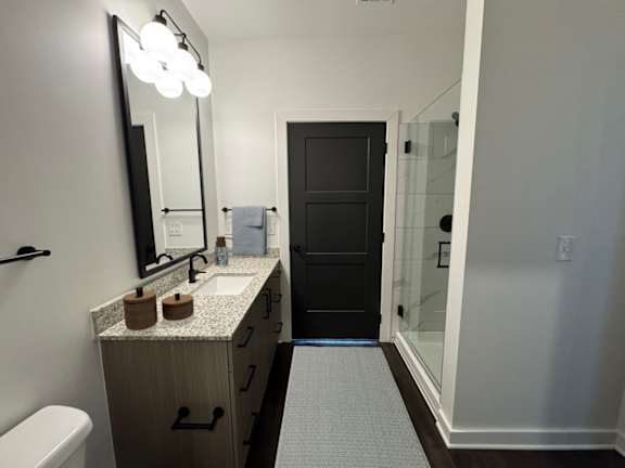 A bathroom with a sink, mirror, toilet and a door.