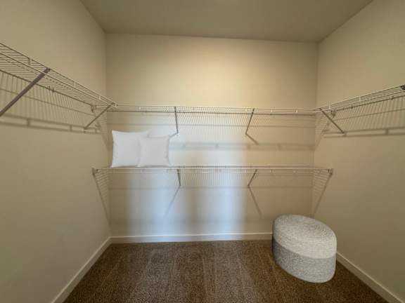 A room with a white bed and a grey ottoman.