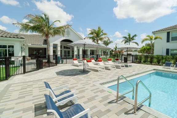 a swimming pool with lounge chairs and umbrellas in front of a house at The Crest at Naples, Naples
