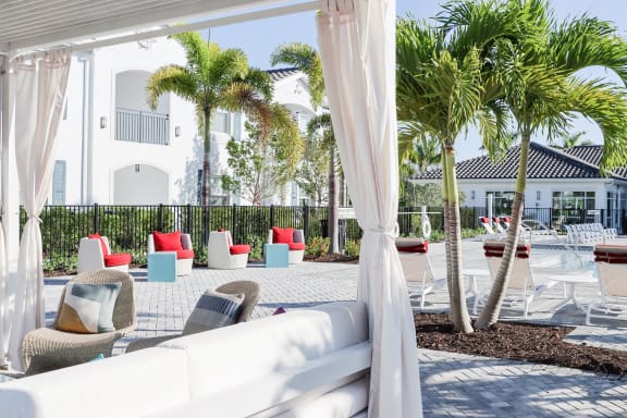 a lounge area with white curtains and chairs and palm trees in the background at The Crest at Naples, Florida