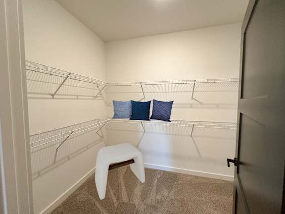 A white chair sits in a corner of a room with a white wall and a white shelf.