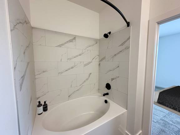 A white bathroom with a marble tile wall and a white bathtub.