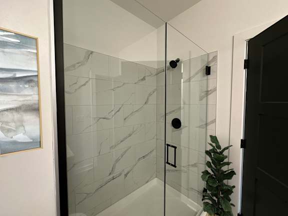 A glass shower stall with a marble tile wall.