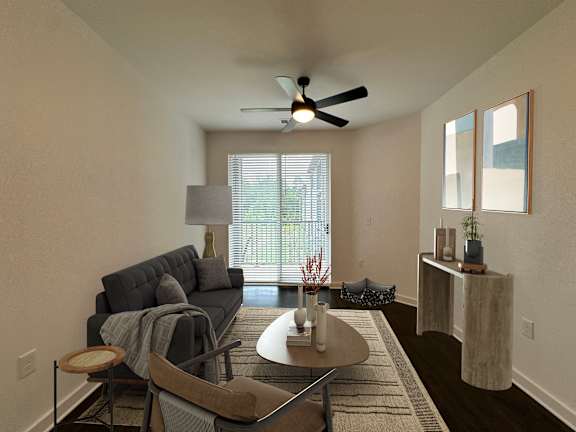 A living room with a grey couch, a brown chair, a round table with a vase and a plant on it, and a ceiling fan.