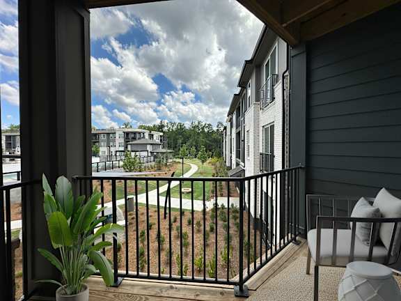 A balcony with a potted plant and a chair overlooking a golf course.